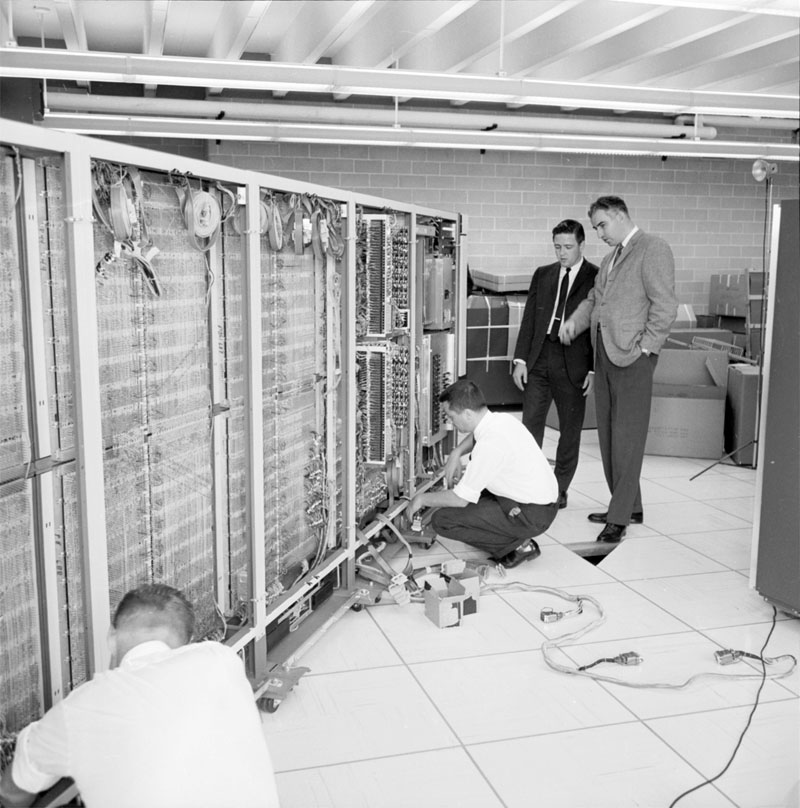 A young Wes Graham talks with colleagues (Chet Warthol and Dave Stiles of IBM) as one works on the installation of the 7040-1401 model IBM computers.